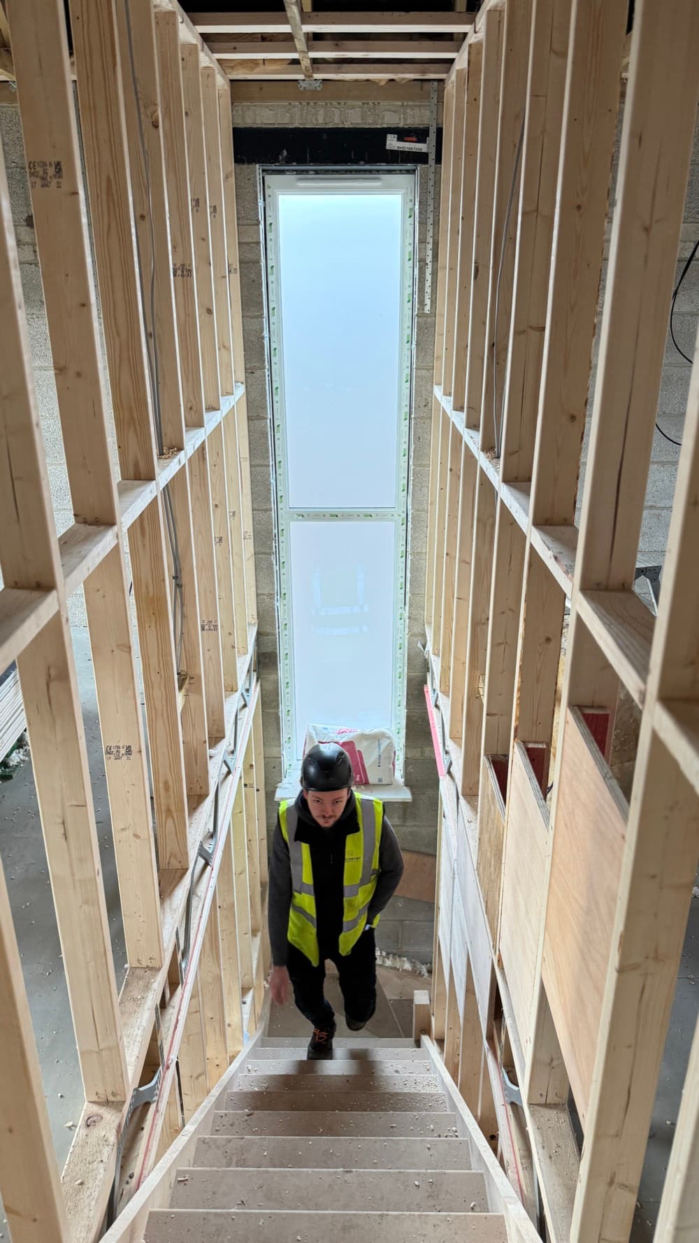 A timber-framed stairwell at first fix, cable routes still open between the studs