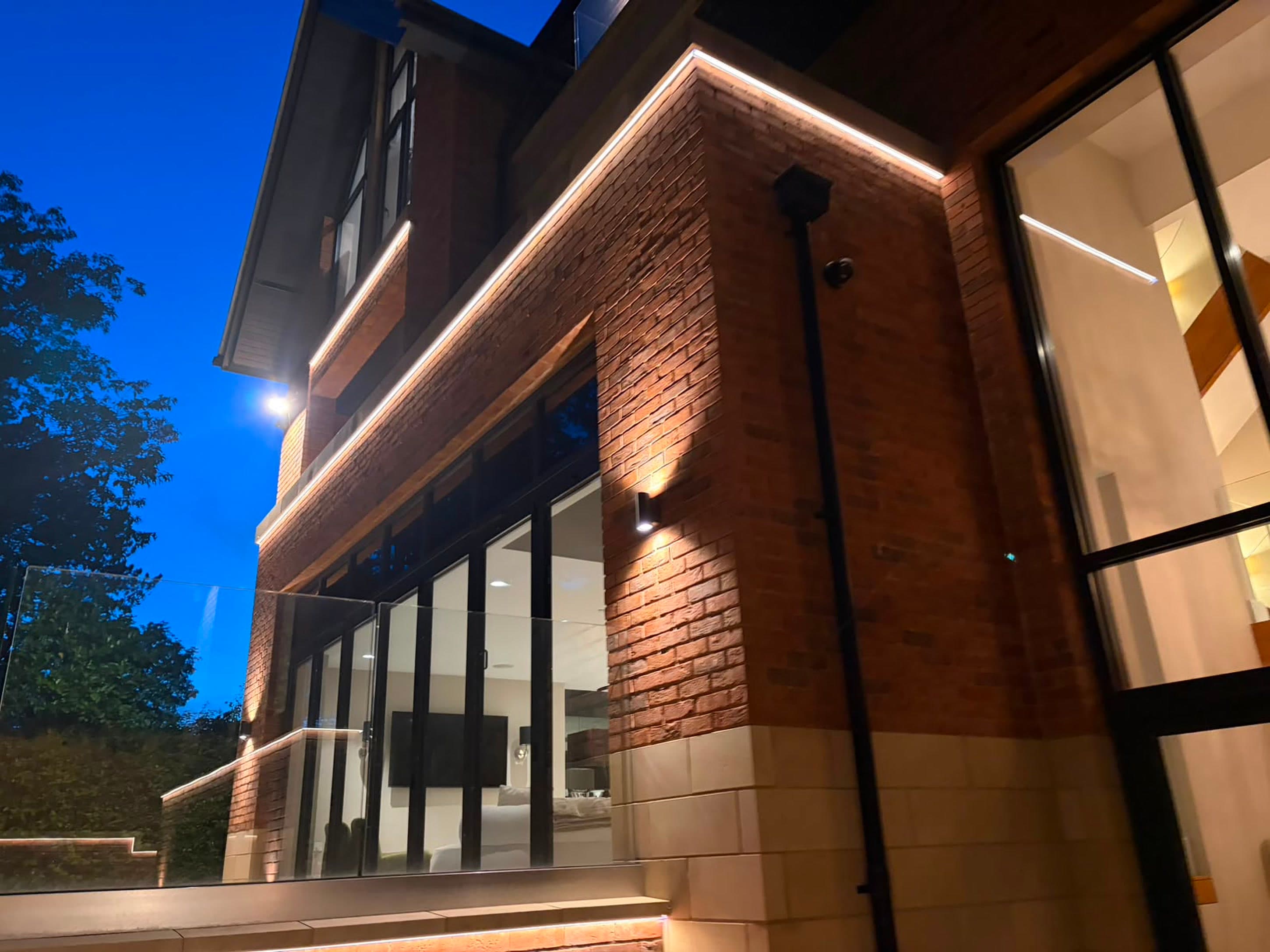 A house at twilight with integrated facade lighting picking out the brickwork, glazing and glass balustrade