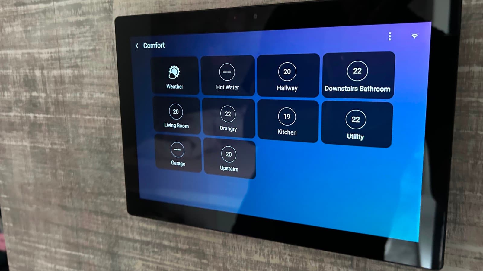 A wall-mounted Control4 touchscreen showing room-by-room heating controls