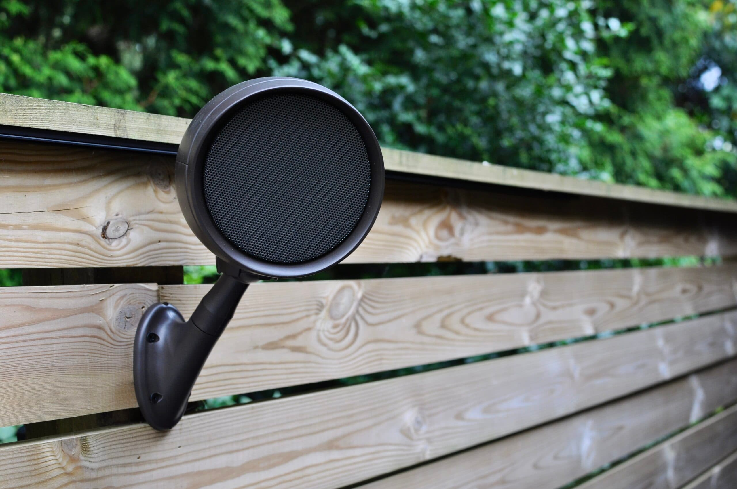 A weatherproof garden speaker mounted on a timber fence beside planting